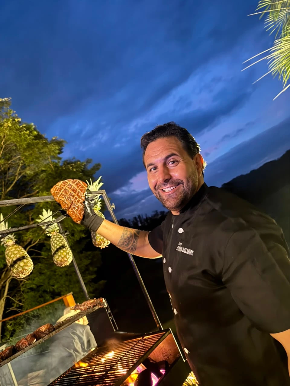 Chef Flávio apresentando abacaxi assado diante da estação de fogo à noite